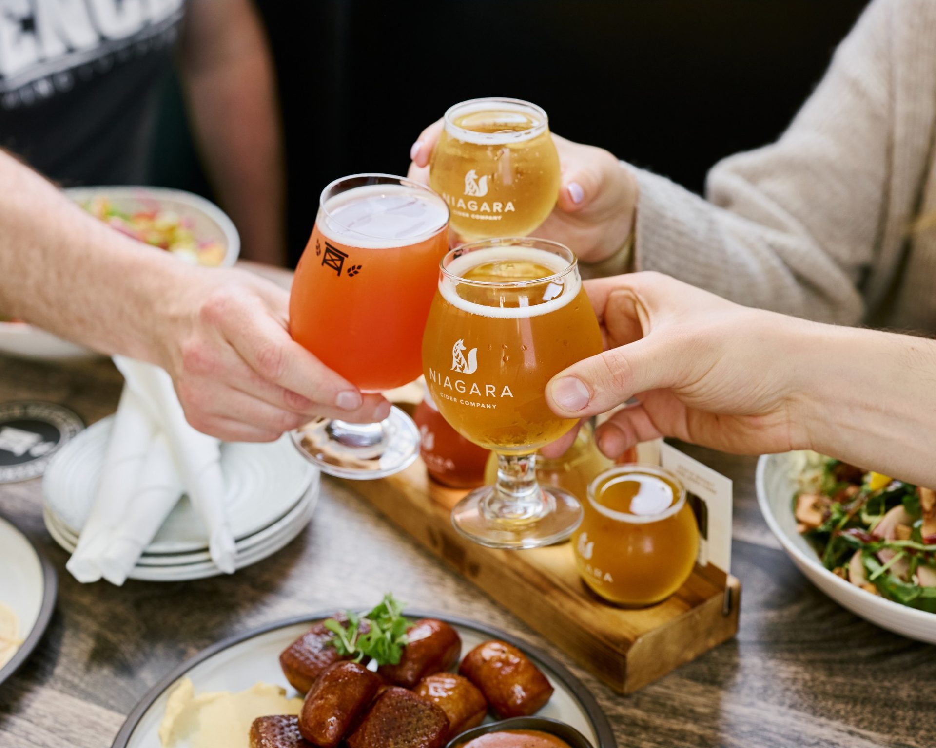 Friends clinking glasses of Niagara Cider Company cider over a shared table