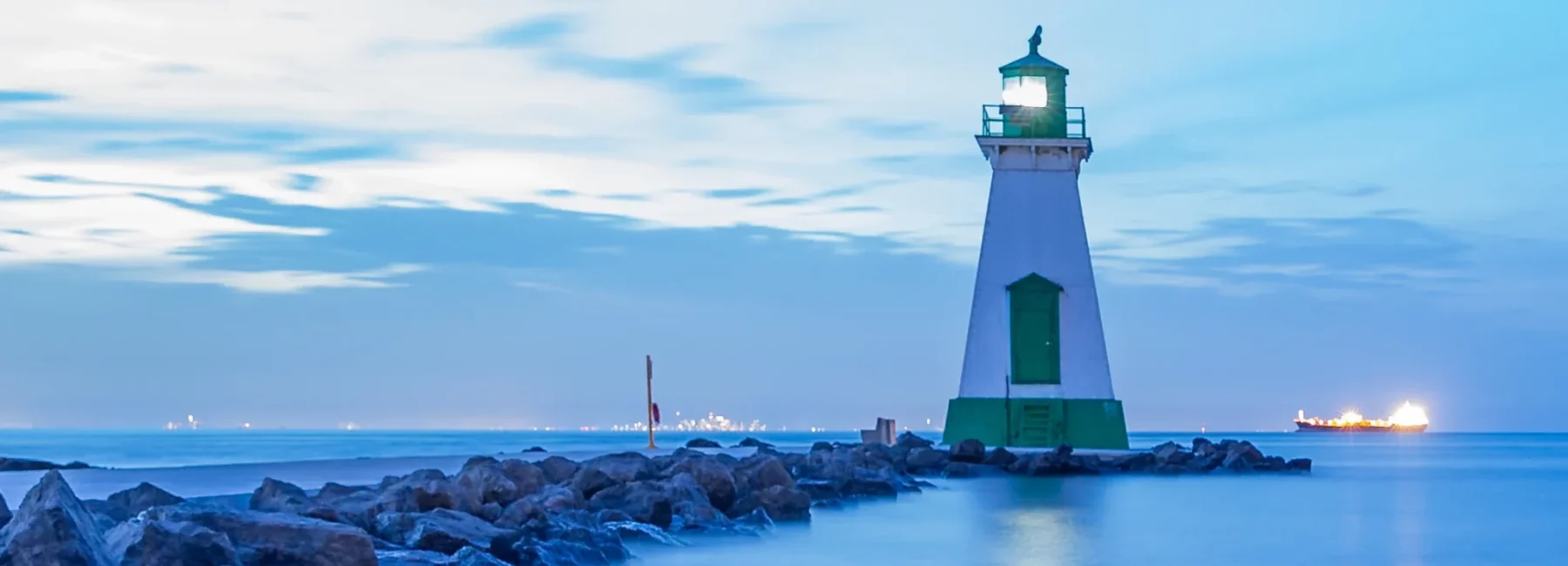 A picturesque lighthouse on the lakefront, surrounded by dramatic rock cliffs, peaceful walking trails, and sandy beaches.
